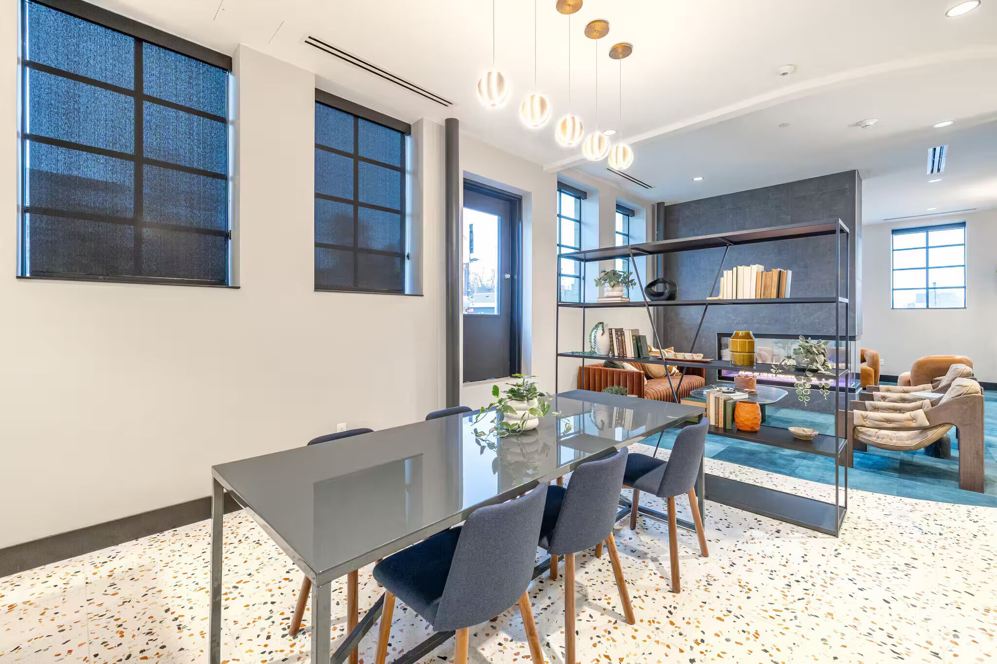 A modern meeting room with a glass table, chairs, a bookshelf, and a sofa.