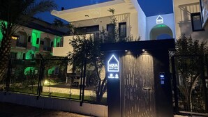 A modern building with a prominent 'AQUA' sign, a gated entrance, and a security keypad. - SUNSET SUİTE 2+1 Family Apartment - 200m Walking Distance to the Beach (Kemer)