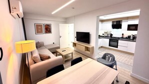 A modern apartment with a living area, dining table, sofa, TV, kitchen, and a small balcony. - SUNSET SUİTE 2+1 Family Apartment - 200m Walking Distance to the Beach (Kemer)
