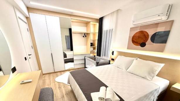 A hotel room with a bed, a desk, a chair, a wardrobe, and a mirror. - SUNSET SUİTE 2+1 Family Apartment - 200m Walking Distance to the Beach (Kemer)
