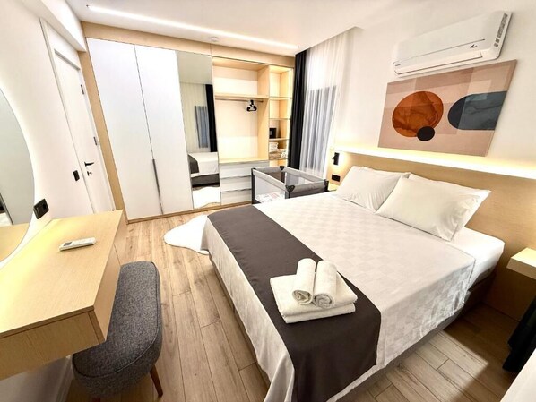 A hotel room with a bed, a desk, a chair, a wardrobe, and a mirror.