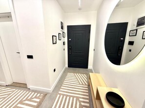 A hallway with a black door, a mirror, and a wooden bench.