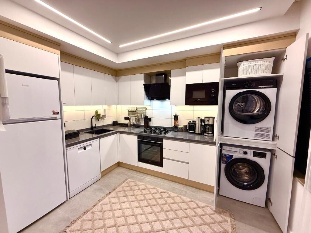 Een moderne keuken met witte kasten, een ingebouwde oven, een magnetron en een wasmachine.