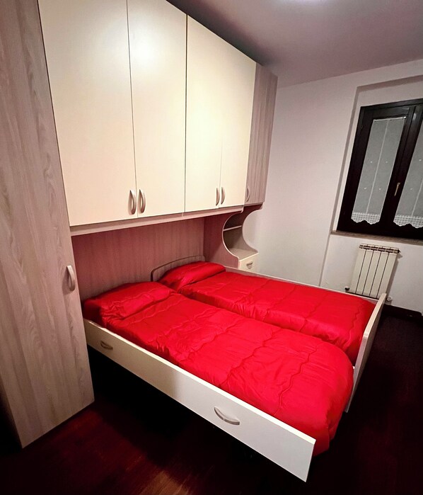 Un dormitorio con cama, armario, ventana y radiador.