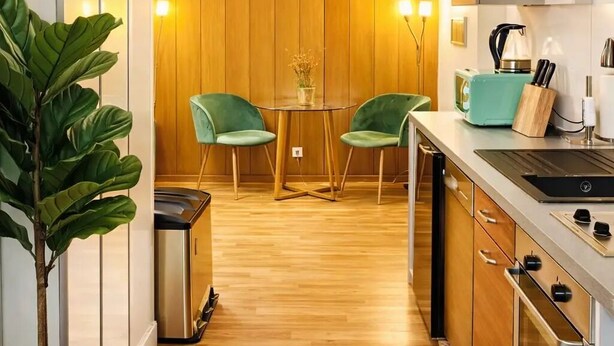 A modern kitchen with wooden paneling, a dining area with two green chairs, a small table with a vase, and a toaster on the counter. - Cozy Home in Nature Park (Schlangenbad)