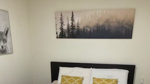 A double bed with white bedding, two pillows with yellow and white patterns, and a painting of a forest on the wall. - Cozy Home in Nature Park (Schlangenbad)