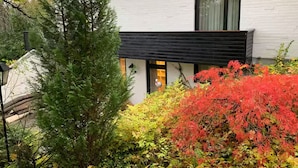 A modern building with a white exterior and black roof, surrounded by dense greenery and autumn foliage. - Cozy Home in Nature Park (Schlangenbad)