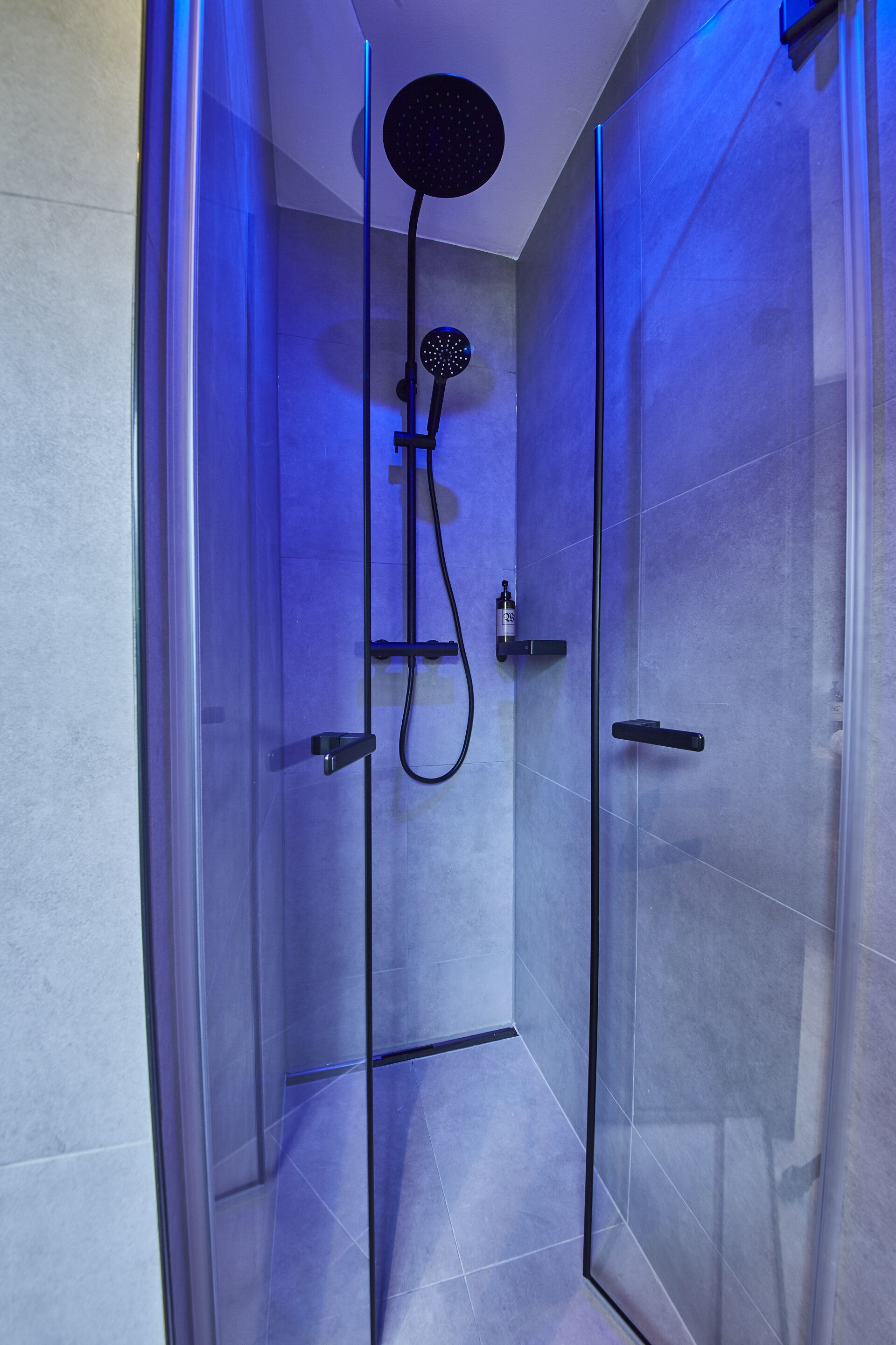 A glass-enclosed shower with a handheld showerhead and a wall-mounted control panel.