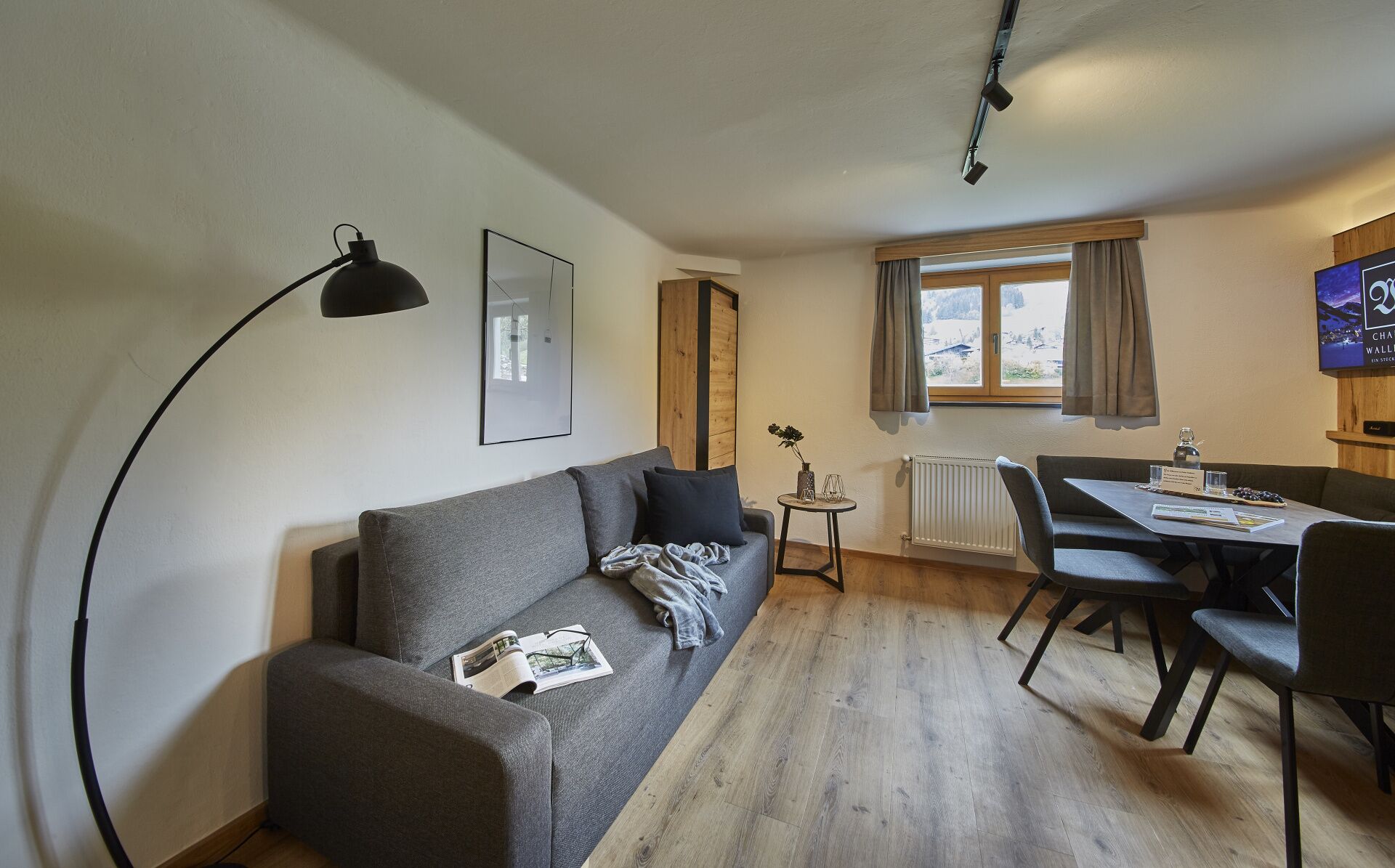 Een moderne woonkamer met een grijze bank, een klein rond tafeltje en een eethoek met tafel en stoelen.