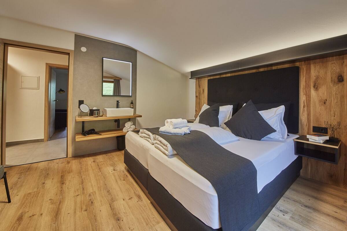 A modern bedroom with a large bed, a bedside table, a mirror, and a built-in shelf with toiletries.