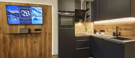 A modern kitchen with dark cabinetry, a built-in oven, and a wooden accent wall.