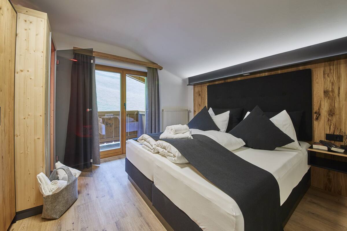 A bedroom with a large bed, a wooden wardrobe, a window with curtains, and a view of the outdoors.