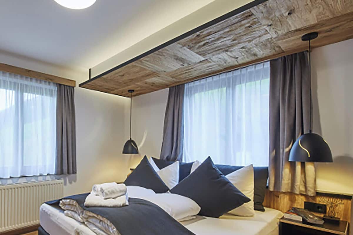 A modern bedroom with a large bed, wooden ceiling beams, and a nightstand with a lamp.