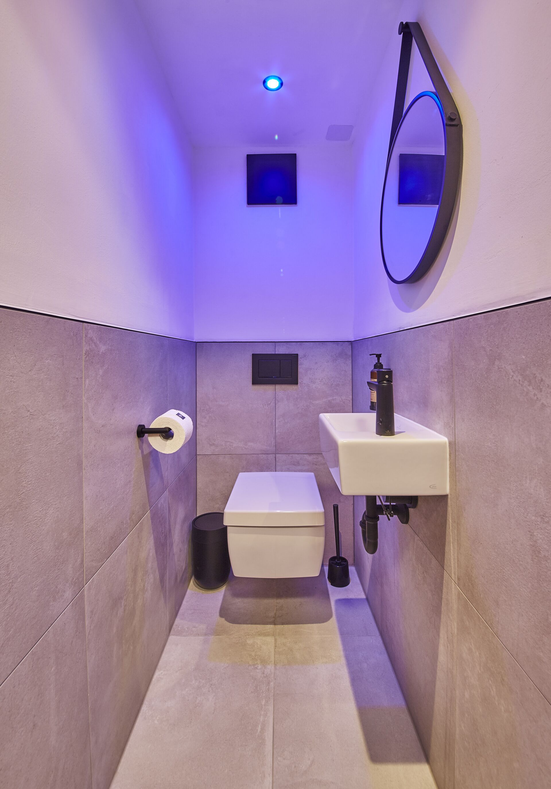 A narrow bathroom with a toilet, sink, and mirror.