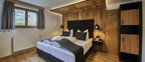 A bedroom with a bed, bedside tables, a nightstand, a radiator, a window with curtains, and a view of the outdoors.