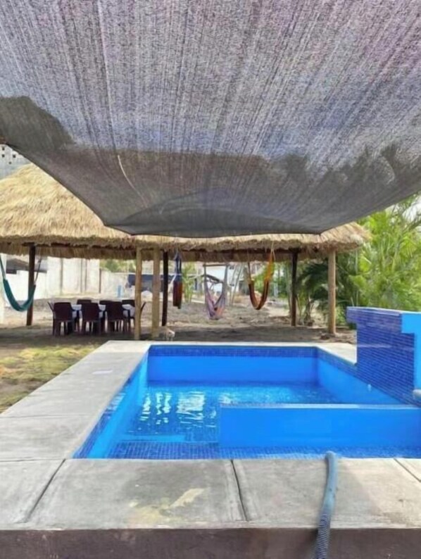 Une piscine dotée d’une structure de toit en chaume, d’un espace détente et d’un hamac.