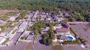 Ett flygbildsbild av ett semesterområde med flera byggnader i bungalowstil, ett centralt poolområde och tät vegetation runt omkring.