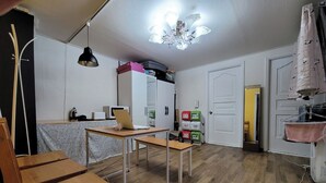 Une pièce avec une table en bois, un bureau avec un ordinateur portable, un ventilateur de plafond et une porte donnant sur une autre pièce.
