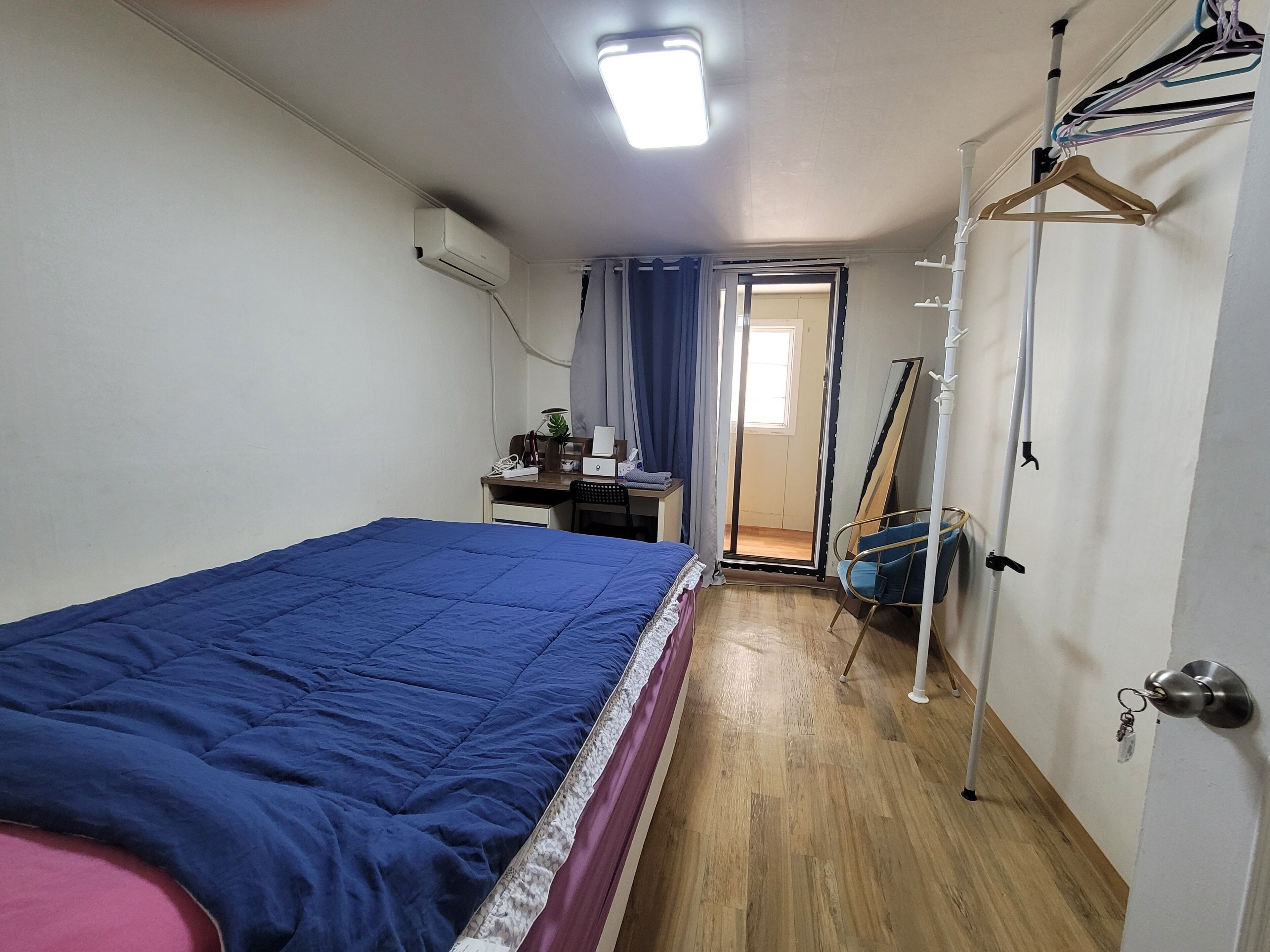 A bedroom with a bed, desk, chair, and a door leading to another room.