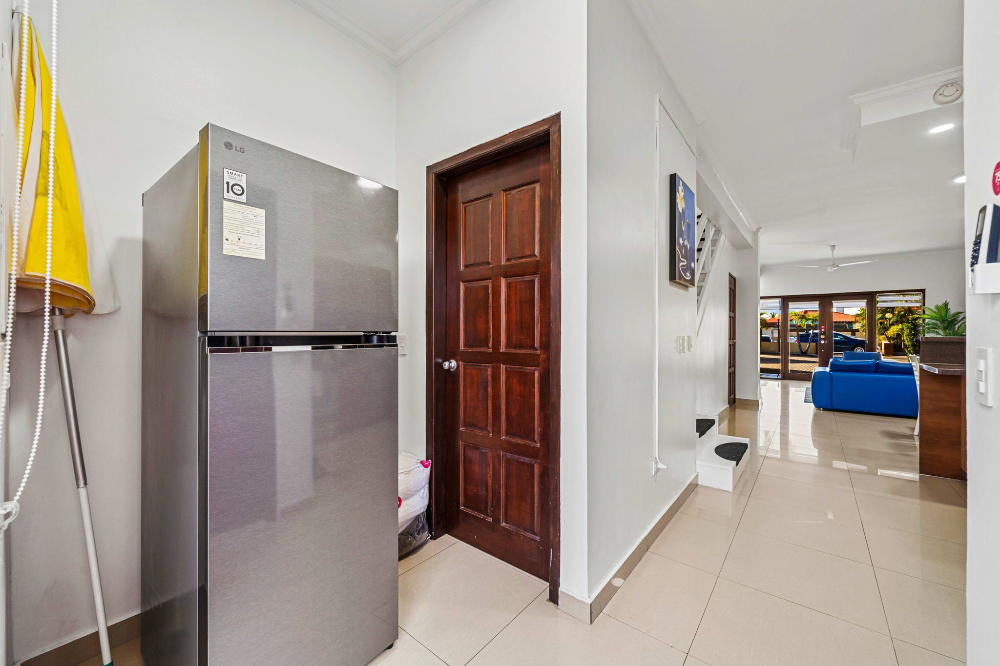 Una cocina moderna con un refrigerador de acero inoxidable, una puerta de madera y un pasillo que conduce a una sala de estar con un sofá azul.