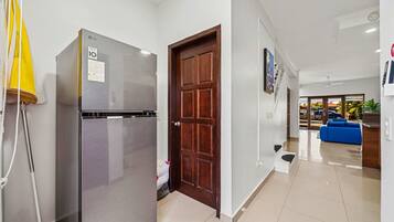 Una cocina moderna con un refrigerador de acero inoxidable, una puerta de madera y un pasillo que conduce a una sala de estar con un sofá azul.
