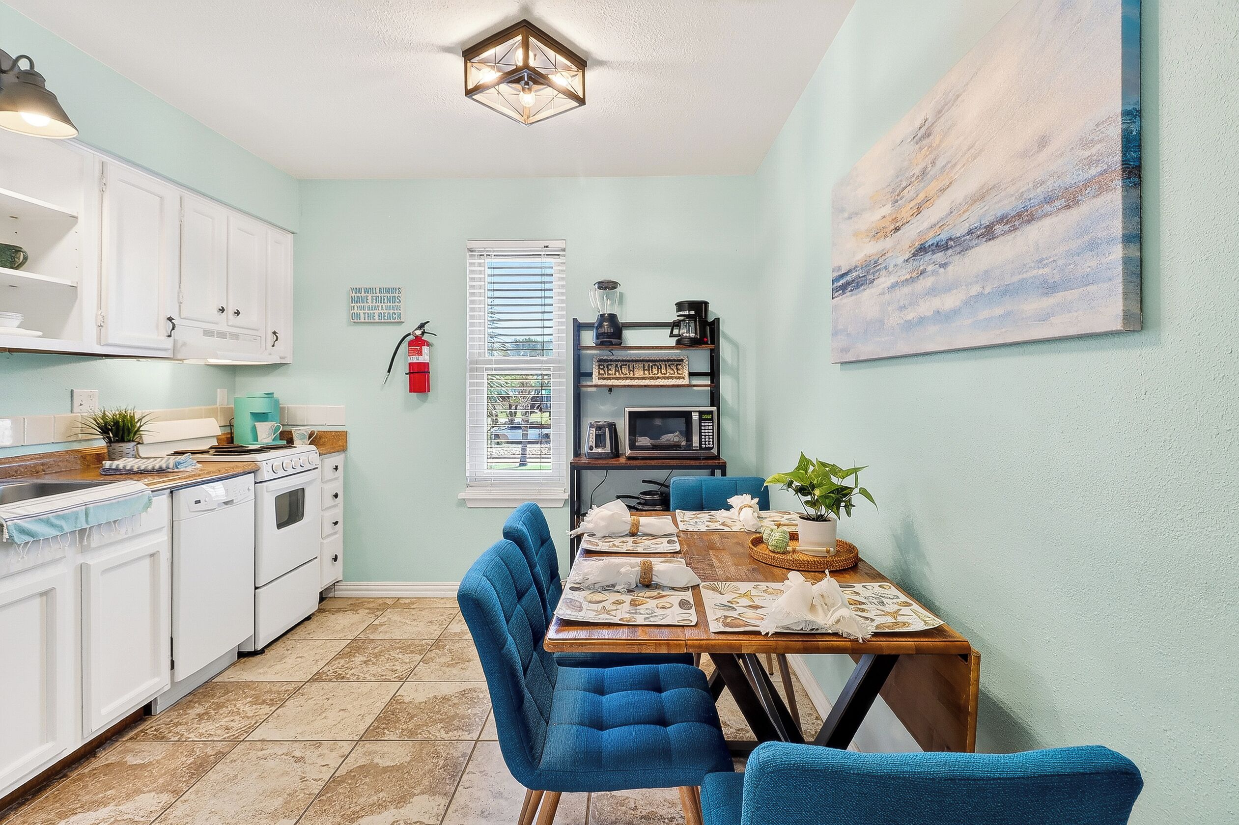 A kitchen with white cabinets, a dining table set for four, and a painting on the wall.