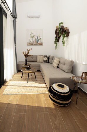 A modern living room with a sectional sofa, a round coffee table, a side table, a hanging plant, and a wall-mounted shelf.