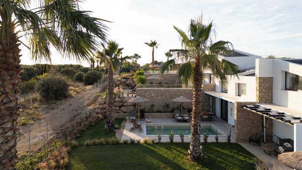 Eine moderne Villa mit Schwimmbad, Sitzgelegenheiten im Freien und Palmen.