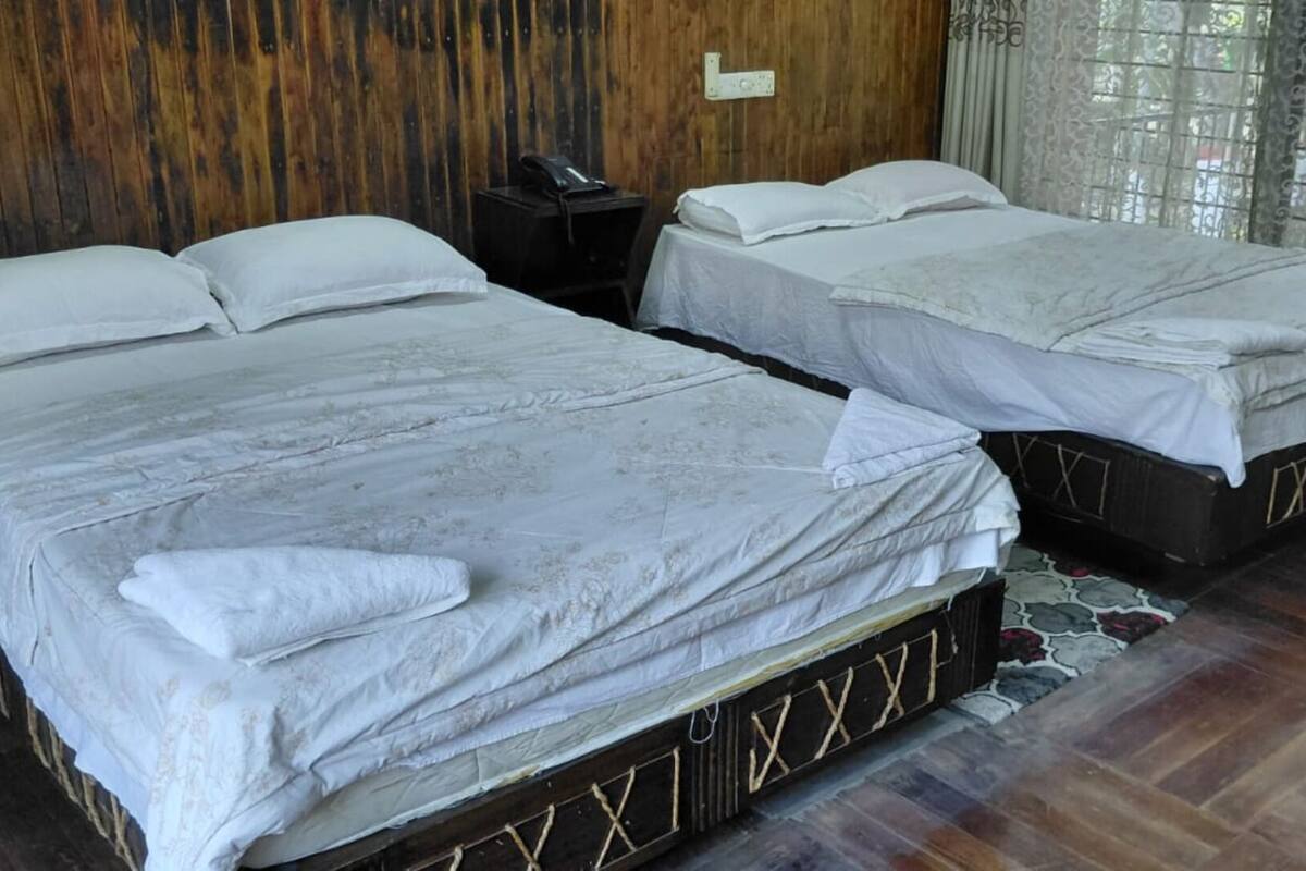 Dos camas individuales con sábanas blancas, una pared de madera, una mesita de noche con teléfono y una alfombra estampada.