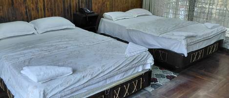 Deux lits simples avec du linge de lit blanc, un mur en bois, une table de chevet avec un téléphone et un tapis à motifs.
