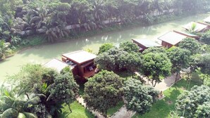 A riverside hotel with multiple wooden buildings, a paved walkway, and lush greenery. - Pubail Resort Club (Gazipur)