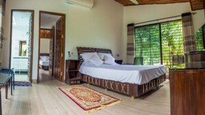 A bedroom with a bed, a desk, a chair, a window with a view of greenery, and a door leading to another room. - Pubail Resort Club (Gazipur)