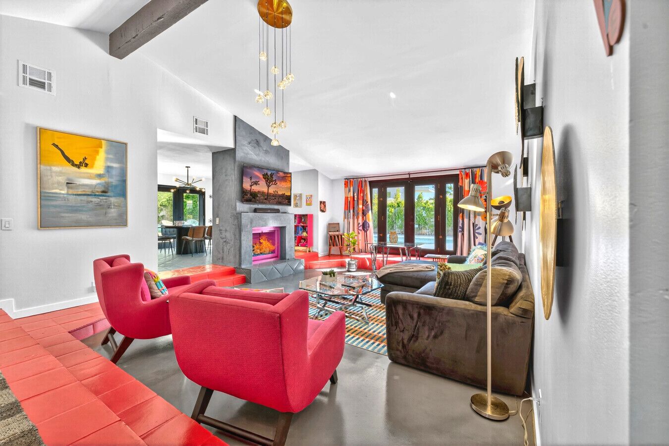 Un salon moderne avec des meubles rouges et gris, une cheminée et de grandes fenêtres.