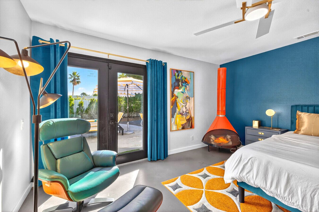 A modern hotel room with a large bed, a seating area with a chair, a fireplace, and a view through the glass door.