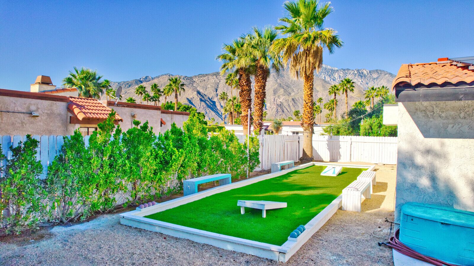 A backyard with a green lawn, a ping pong table, and palm trees.