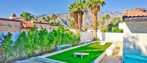 A backyard with a green lawn, a ping pong table, and palm trees.