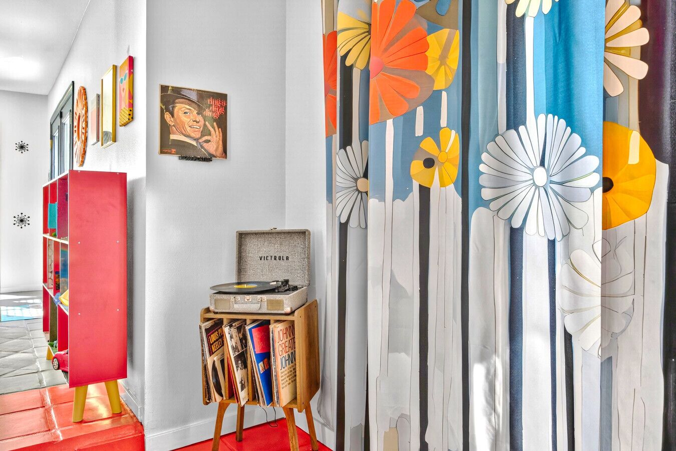 Een gang met een rode boekenkast, een platenspeler en een muur met een bloemenmotief.