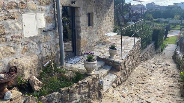 A stone building with a rustic exterior, a metal door, and a small outdoor seating area with a chair and table. - Charming bed and breakfast in an authentic Ardèche farmhouse. (Saint-Paul-le-Jeune)