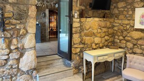 A stone-walled room with a television mounted on the wall, a wooden table, and a chair. - Charming bed and breakfast in an authentic Ardèche farmhouse. (Saint-Paul-le-Jeune)