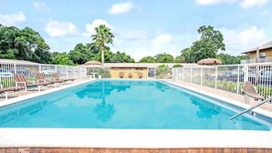 Ein rechteckiger Pool mit weißem Zaun, Liegestühlen und einer Palme im Hintergrund.