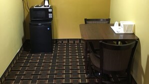 Una habitación pequeña con una mesa, sillas, microondas y cafetera.