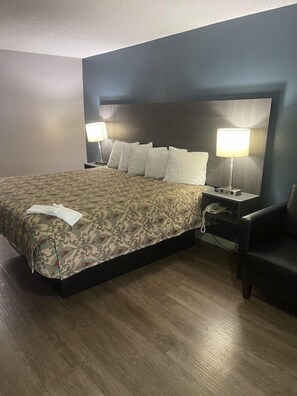 Ett hotellrum med en stor säng, två sänglampor, en stol och ett sidobord med en telefon.