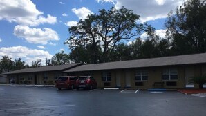 Ein Motel mit Parkplatz, zwei rote Autos parkiert, und ein großer Baum im Hintergrund.