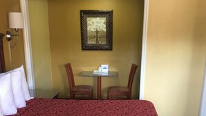Ein Hotelzimmer mit einem großen Bett, einem kleinen Tisch mit einem weißen Gegenstand, zwei Stühlen und einem gerahmten Bild an der Wand.