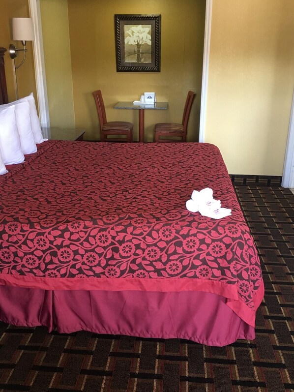 A hotel room with a large bed, a small table with a white object, two chairs, and a framed picture on the wall. - Days Inn by Wyndham Orange City/deland (Orange City)