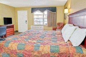 Een hotelkamer met een bed, een bureau met een televisie, een stoel, een raam met gordijnen en een wandlamp.