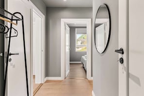 Un pasillo con piso de madera, puertas blancas y vista a un dormitorio con cama y ventana.