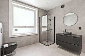 Un baño moderno con ducha envuelta en vidrio, un espejo redondo y un tocador de tonos oscuros.