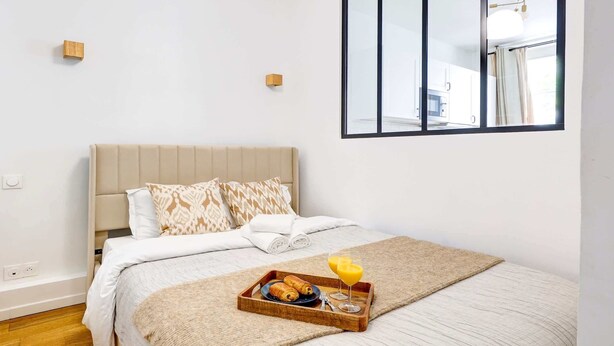 Un lit bien fait, avec un plateau de petit-déjeuner à proximité, une fenêtre donnant sur l’extérieur et un luminaire moderne.