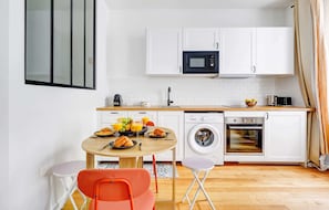 Una cocina compacta con armarios blancos, microondas, lavadora y horno.
